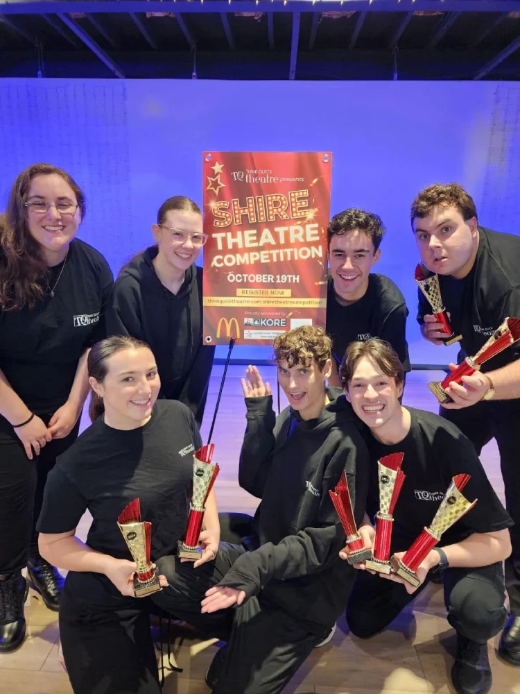 Group of theatre performers celebrating with trophies at the Shire Theatre Competition after receiving awards on stage.